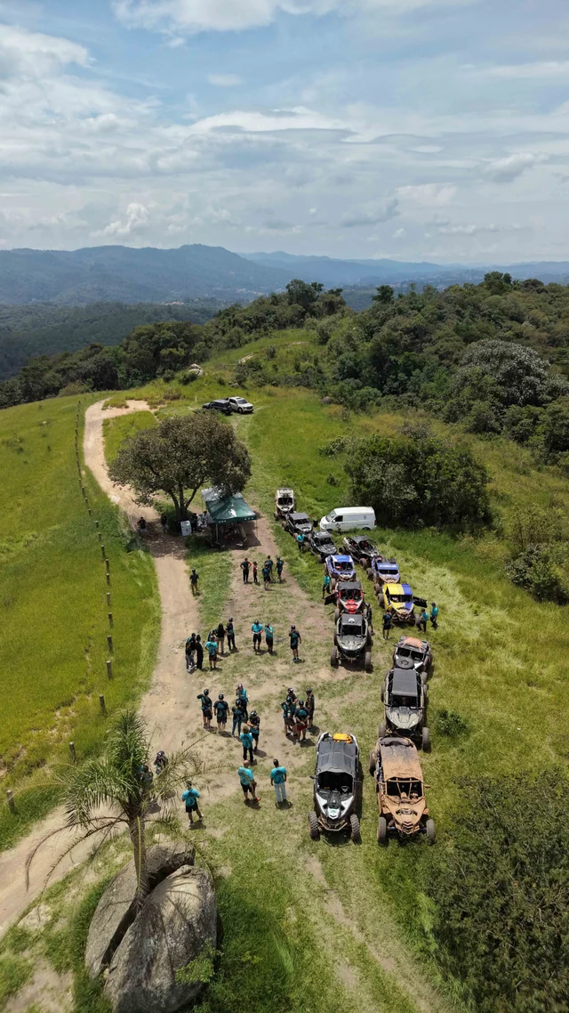 Vista aérea vertical de UTVs e participantes em área aberta de trilha.