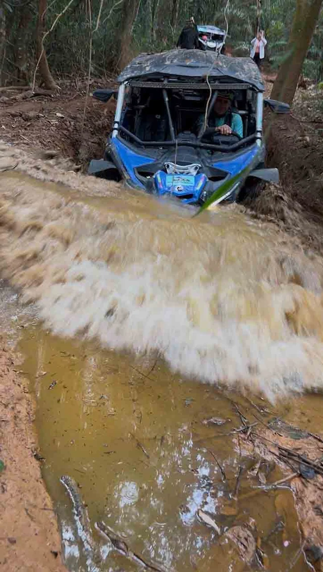 UTV atravessando água em uma trilha estreita.